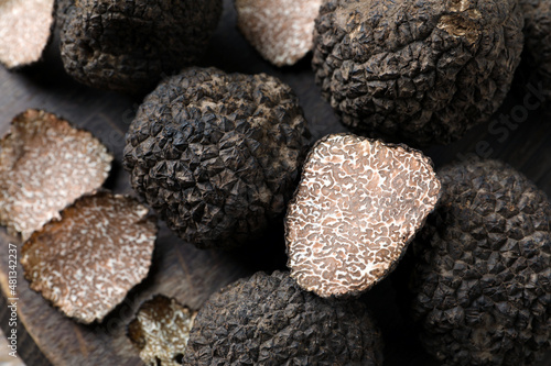Whole and cut black truffles on wooden board, top view