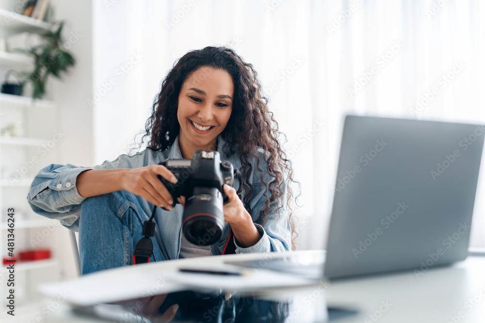 Female Photographer Holding Camera Looking At Photos Using Laptop Indoors Female Photographer Holding Camera Looking At Photos Using Laptop Indoors