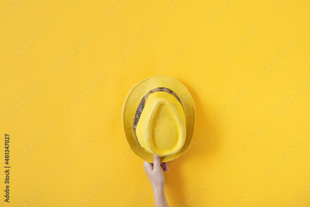 Female hand holding yellow straw hat on yellow background