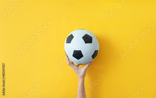 Female hand holding soccer ball on yellow background
