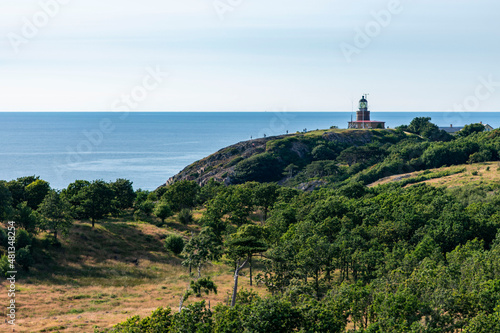 Fototapeta Naklejka Na Ścianę i Meble -  Kullaberg fyr, old lighthouse on the cliffs of Kullaberg naturreservat on the Swedish west coast. Lighthouse on the rocks viewing out into the baltic sea. Warm summer, high cliffs, deap ocean. Trees