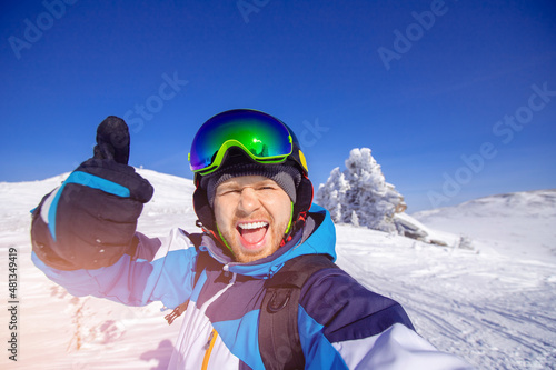 Winter recreation on nature ski tour, smile man skier makes selfie photo on background of snowy forest in mountains sunny