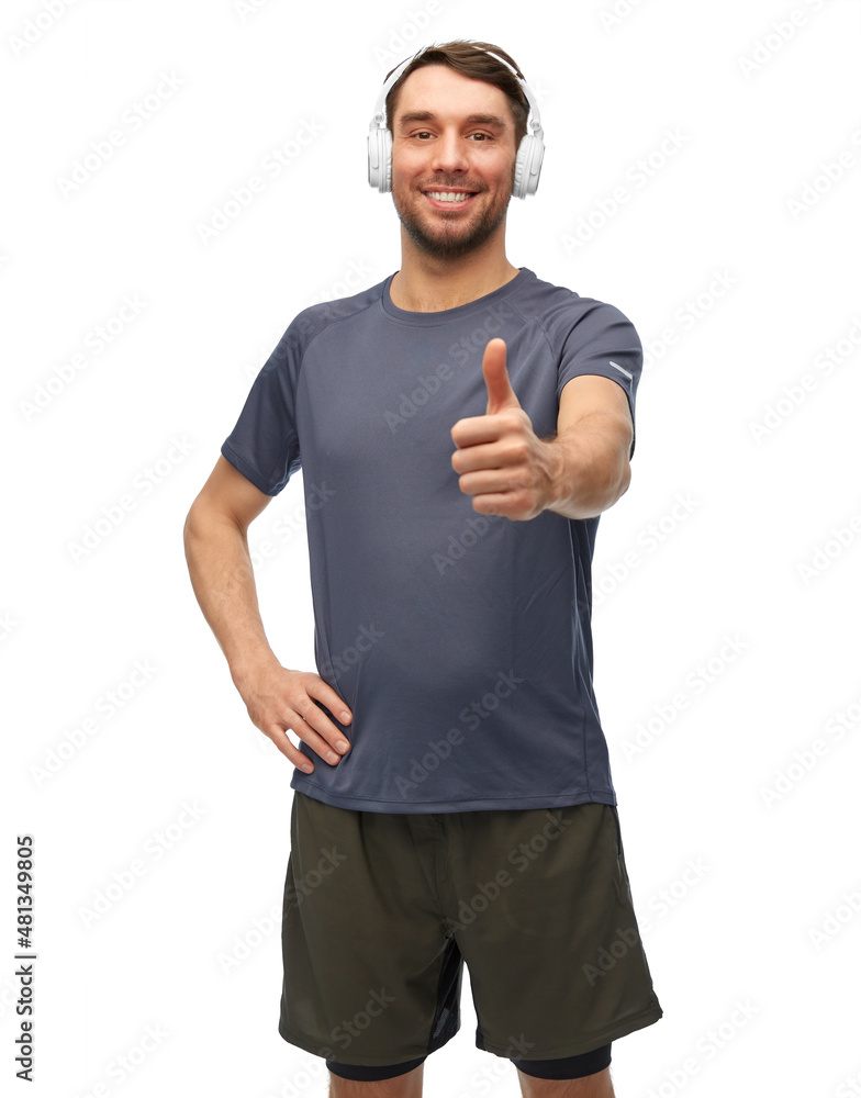Fototapeta premium fitness, sport and healthy lifestyle concept - smiling man in sports clothes with headphones listening to music and showing thumbs up over white background