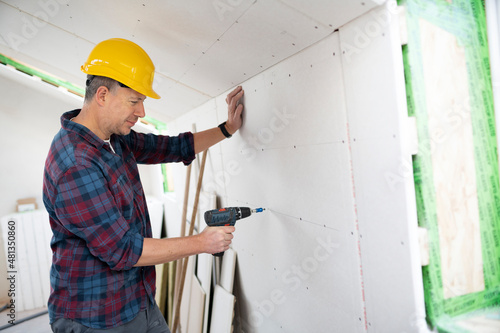 drywall worker with yellow safety helmet works on building site in a house