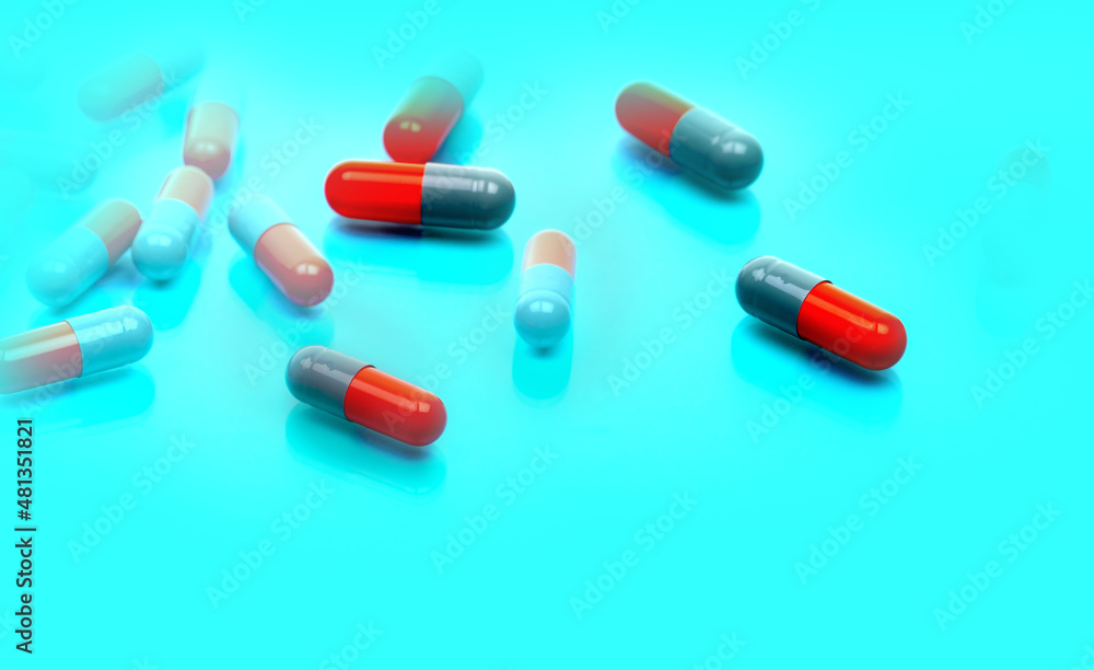 Selective focus on gray-orange antibiotic capsule pills on blue background. Pharmaceutical industry. Toxicology and pharmacology concept. Antibiotic drug resistance. Capsule pills manufacturing. Selective focus on gray-orange antibiotic capsule pills on blue background. Pharmaceutical industry. Toxicology and pharmacology concept. Antibiotic drug resistance. Capsule pills manufacturing.