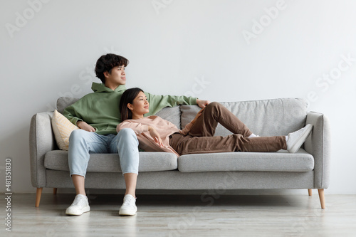 Romantic young Asian couple relaxing on couch in living room, spending time together, copy space