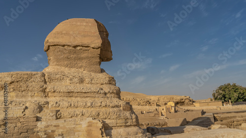 A fragment of the sculpture of the Great Sphinx. Profile view against the blue sky. Close-up. In the distance you can see the ruins of an ancient temple. Egypt. Giza