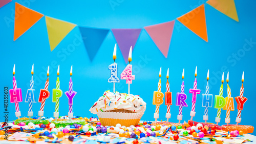 Candle letters word happy birthday to a child with the number fourteen on a beautiful blue background. Copy space Happy birthday greetings for 14 years old, lit candles with holiday decorations. 