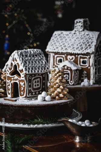Chocolate and dried fruit cake decorated with handmade gingerbread house and lemon cookie spruces with Christmas tree on background.
