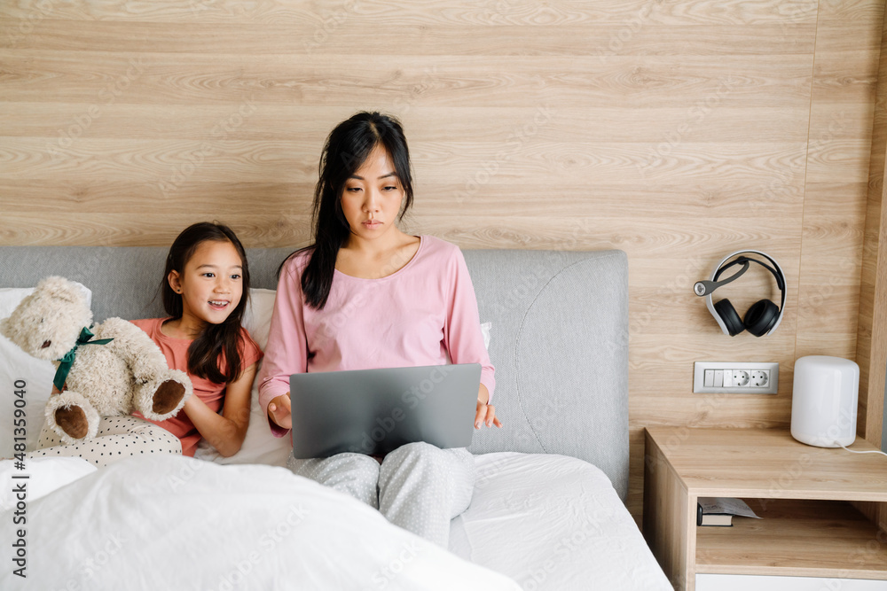 Asian mother and daughter using laptop while sitting on bed Asian mother and daughter using laptop while sitting on bed