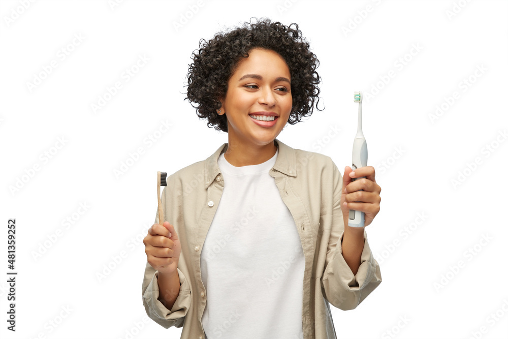 eco living, zero waste and sustainability concept - portrait of happy smiling young woman comparing wooden and electric toothbrushes over white background eco living, zero waste and sustainability concept - portrait of happy smiling young woman comparing wooden and electric toothbrushes over white background