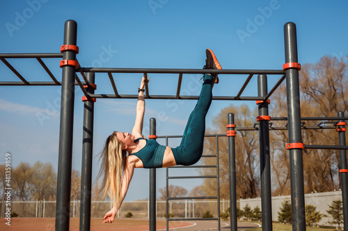 Athletic woman is exercising, having fun on the horizontal bar in spring outdoors.