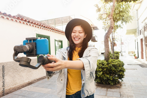Happy asian influencer girl having fun vlogging with gimbal and mobile phone outdoor - Focus on face photo