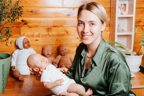 Принти на полотні Portrait of happy caucasian young woman holding realistic newborn baby reborn doll in her arms and looking at camera, indoors