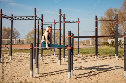 Sporty woman is working out on the horizontal bar in spring outdoors.