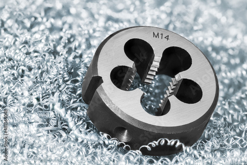 Close-up of steel solid threading die on metal swarf background. Round metric tool to precise cutting external thread on cylindric rods or bolts lying in heap of spiral twisted chips. Selective focus.