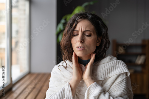 Upset sick woman standing at home touching swollen glands, having pain or scratchy sensation in throat, selective focus. Female suffering from angina or tonsillitis caused by infection or irritation photo