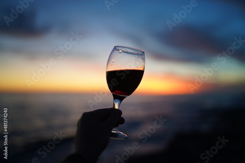 Close up on hands holding red wine glasses on the beach during sunset, celebration concept
