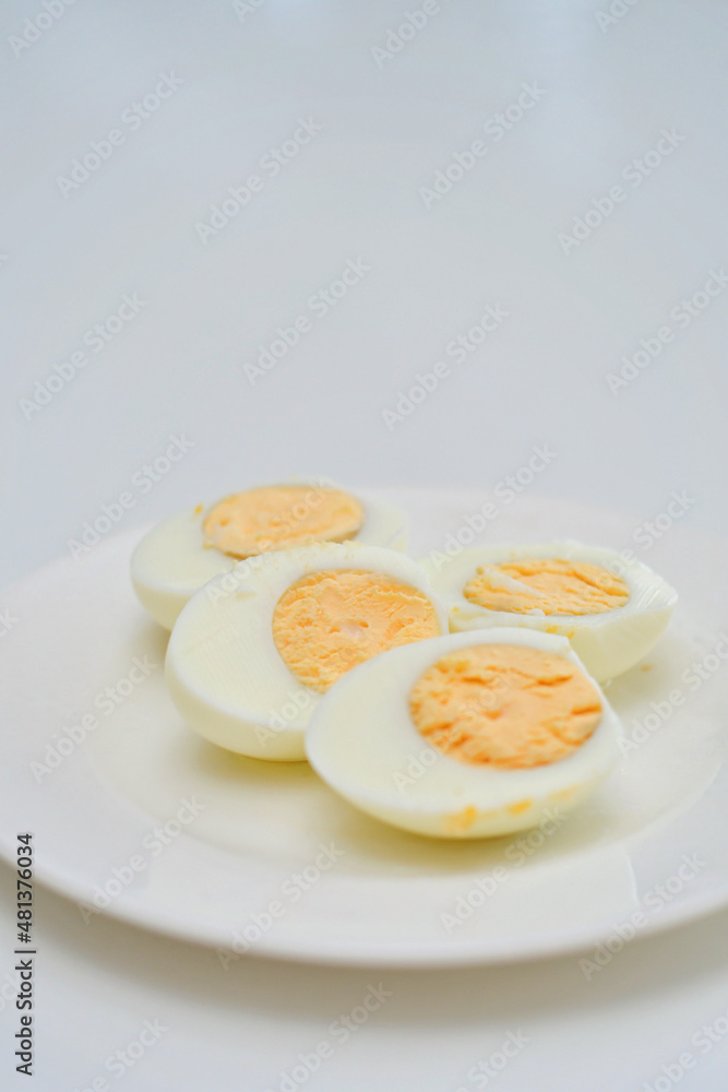 Boiled eggs on a kitchen table, healthy breakfast and protein rich diet. Eggs on a plate with a knife on a side, airy and white background with green plants and a light reflection from the table. Boiled eggs on a kitchen table, healthy breakfast and protein rich diet. Eggs on a plate with a knife on a side, airy and white background with green plants and a light reflection from the table.