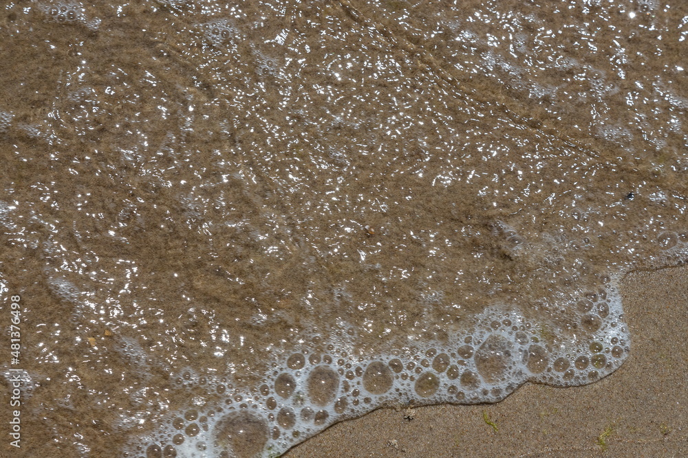 Close-up of sea foam on the sand beach with summer sunlight