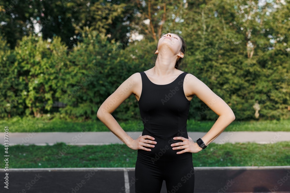 A fitness woman doing a stretching exercise stretches her triceps and shoulders. Women stretch to warm up before running or training. In the park, on the sports field.