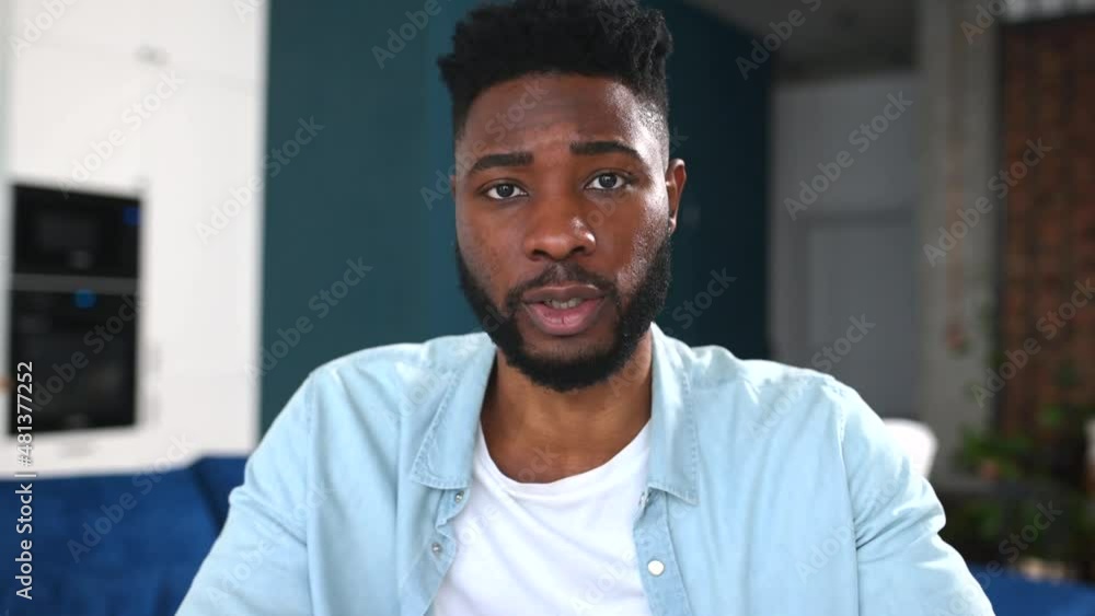 Portrait of happy multiracial man sitting at the sofa and looking at the camera, involved in video meeting. Webcam view of smart male in blue shirt Portrait of happy multiracial man sitting at the sofa and looking at the camera, involved in video meeting. Webcam view of smart male in blue shirt