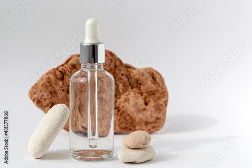 Multi-colored stones with a transparent bottle with a pipette on a white background. Natural podium with cosmetics