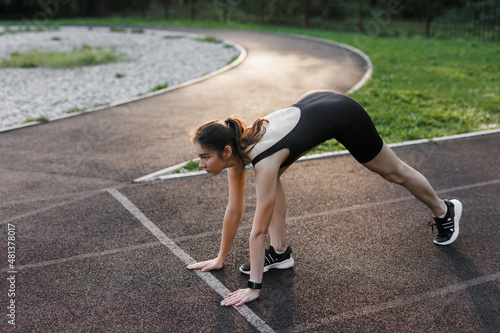 A fitness woman doing a stretching exercise stretches her legs. Women stretch to warm up before running or training. In the park, on the sports field. side view, yoga elements.