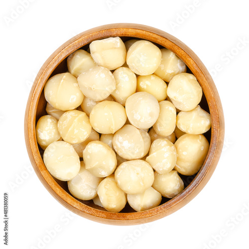 Shelled and dried macadamia nuts, in a wooden bowl. Also called Queensland, bush, maroochi, bauple or Hawaii nut. Wholesome snack. Close-up, from above, isolated on white background, macro food photo.
