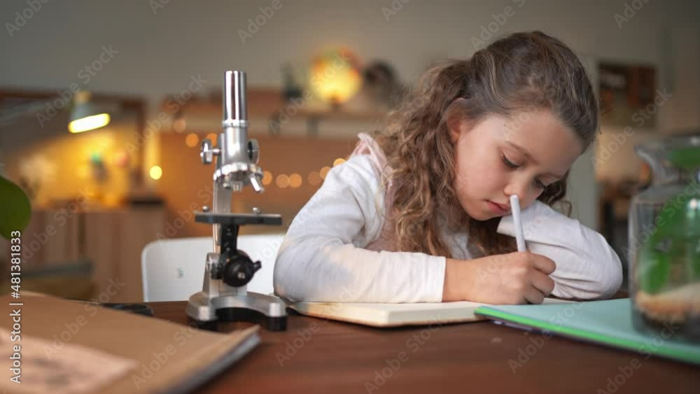 Concentrated little girl writing and making a herbarium, biology project indoors at home, homeschooling. Concentrated little girl writing and making a herbarium, biology project indoors at home, homeschooling.