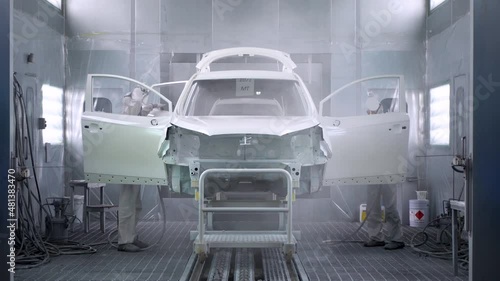 Two men paint a car in a spray booth. Car manufacturing.