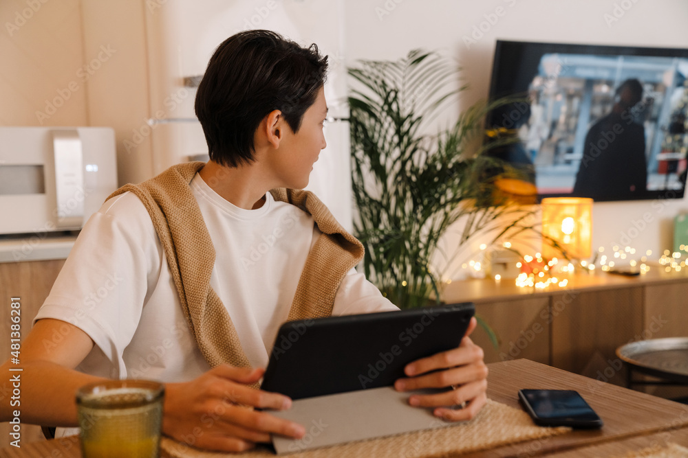 Asian boy using tablet computer while watching tv in kitchen Asian boy using tablet computer while watching tv in kitchen