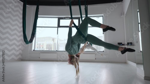 Two young yogi women doing aerial yoga practice in green hammocks in fitness club. Beautiful females working out in class, performing aero yoga. Variation of Parsvottanasana, Pyramid pose photo