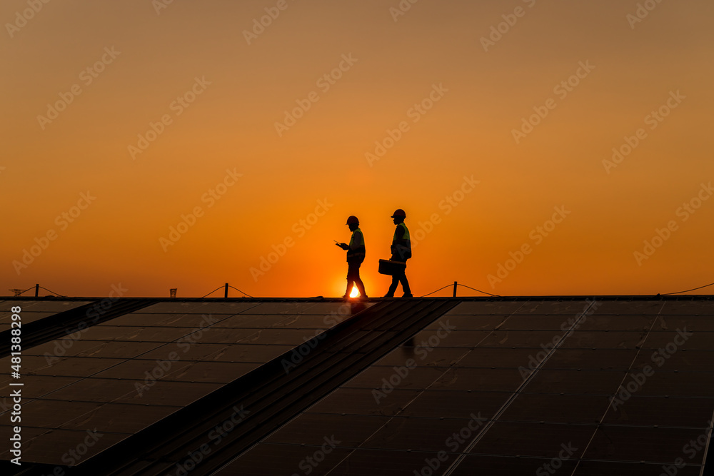 Silhouette engineers walking on roof inspect and check solar cell panel by hold equipment box and radio communication ,solar cell is smart grid ecology energy sunlight alternative power concept.