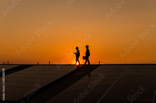 Silhouette engineers walking on roof inspect and check solar cell panel by hold equipment box and radio communication  solar cell is smart grid ecology energy sunlight alternative power concept.