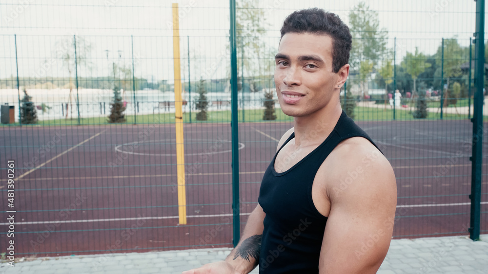 athletic bi-racial man with tattoo looking at camera at outdoors gym.