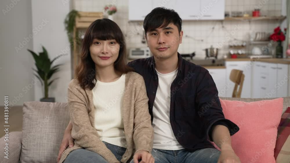 portrait of a young asian married couple smiling and looking at the camera while sitting together on the couch in their new apartment portrait of a young asian married couple smiling and looking at the camera while sitting together on the couch in their new apartment