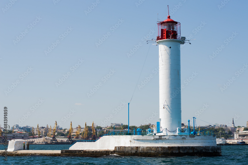 Lighthouse in the sea against the blue sky, in the background the city coast.