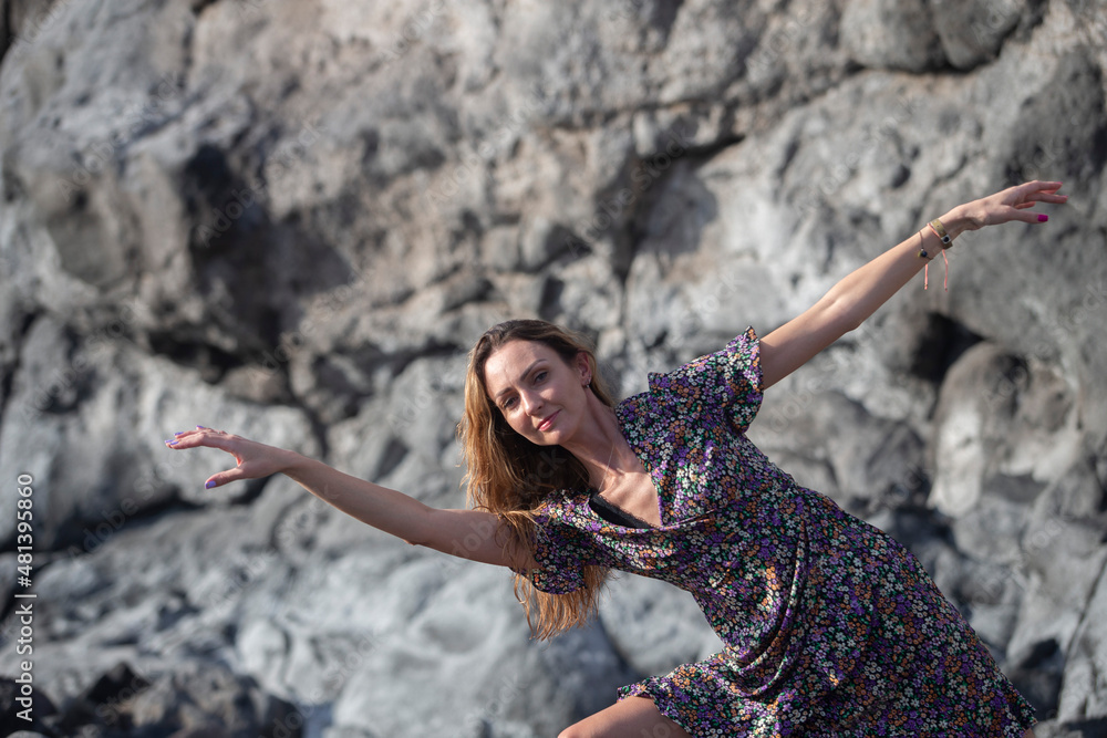 Young beautiful ballerina dancing, posing on rock at beach