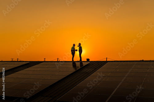 Silhouette engineers walking on roof inspect and check solar cell panel by hold equipment box and radio communication ,solar cell is smart grid ecology energy sunlight alternative power concept.