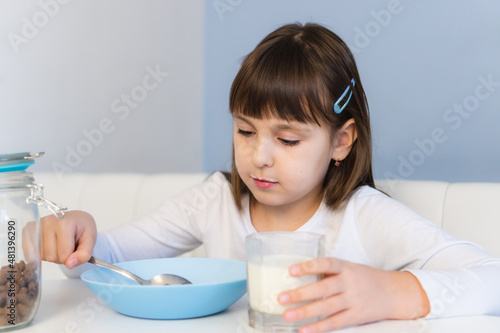 Little girl eats chocolate corn balls with milk sitting at white table. Child have breakfast