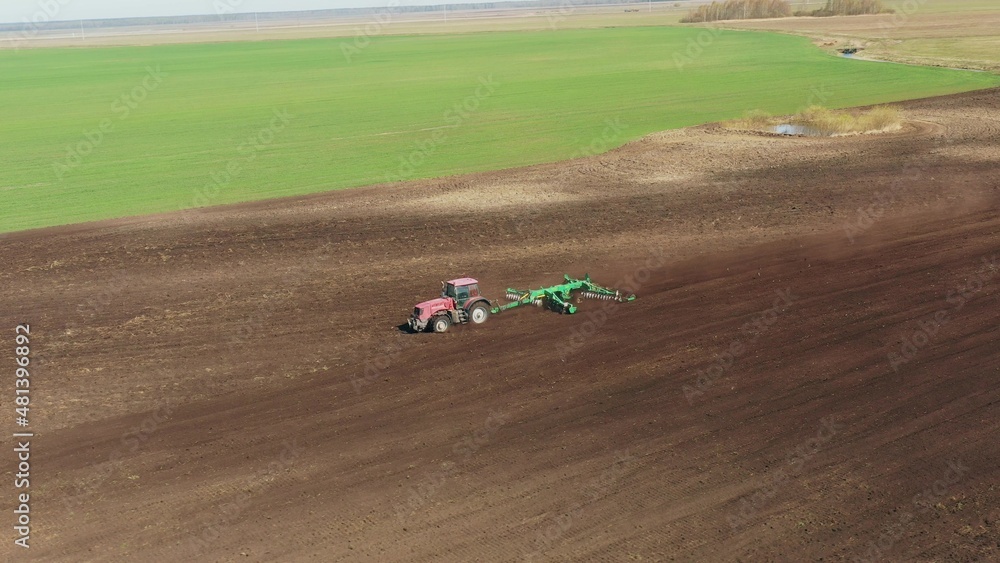 4K Aerial Elevated View.Tractor Plowing Field. Beginning Of Agricultural Spring Season. Cultivator Pulled By A Tractor In Countryside Rural Field Landscape