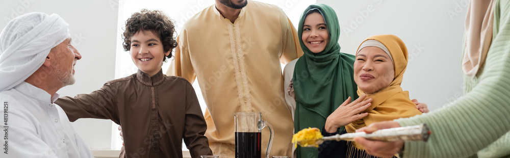 Smiling multiethnic muslim family near woman with pilaf at home, banner. Smiling multiethnic muslim family near woman with pilaf at home, banner.