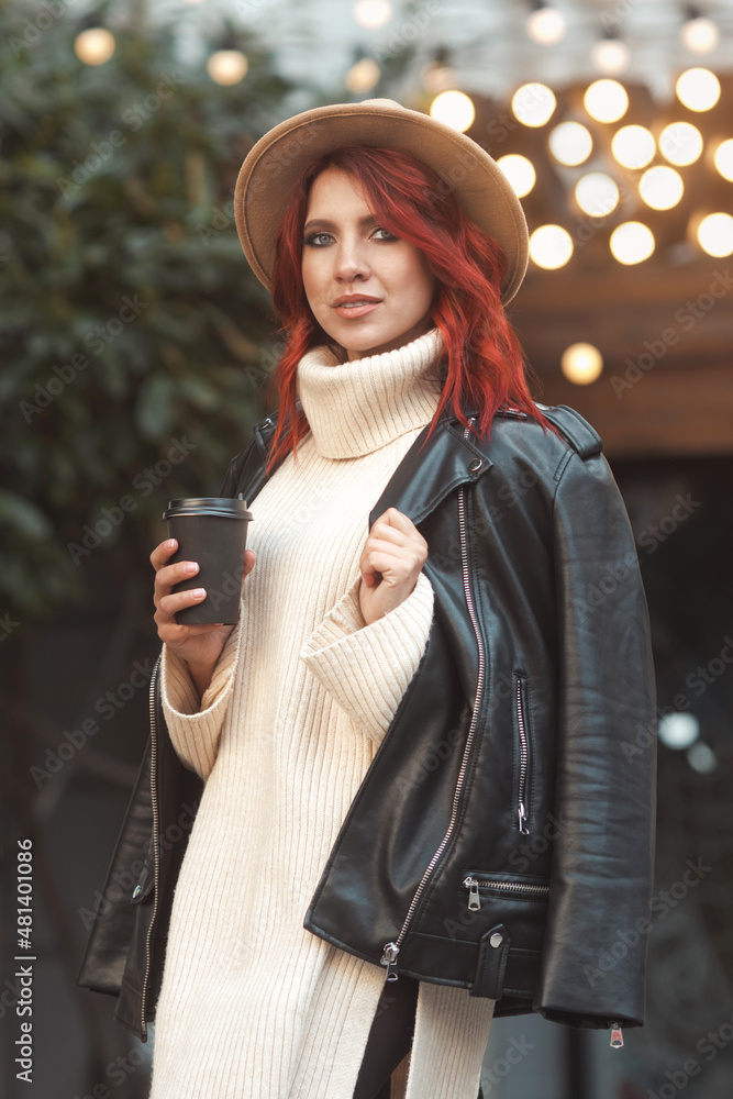 Street style portrait of fashionable and stylish redhead woman 25-30 years old in fashion casual clothes, sitting in cafe outdoors and drinking take away hot coffee from paper cup Street style portrait of fashionable and stylish redhead woman 25-30 years old in fashion casual clothes, sitting in cafe outdoors and drinking take away hot coffee from paper cup