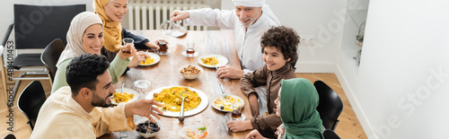 Slika na platnu high angle view of happy multiethnic muslim family having dinner at home, banner
