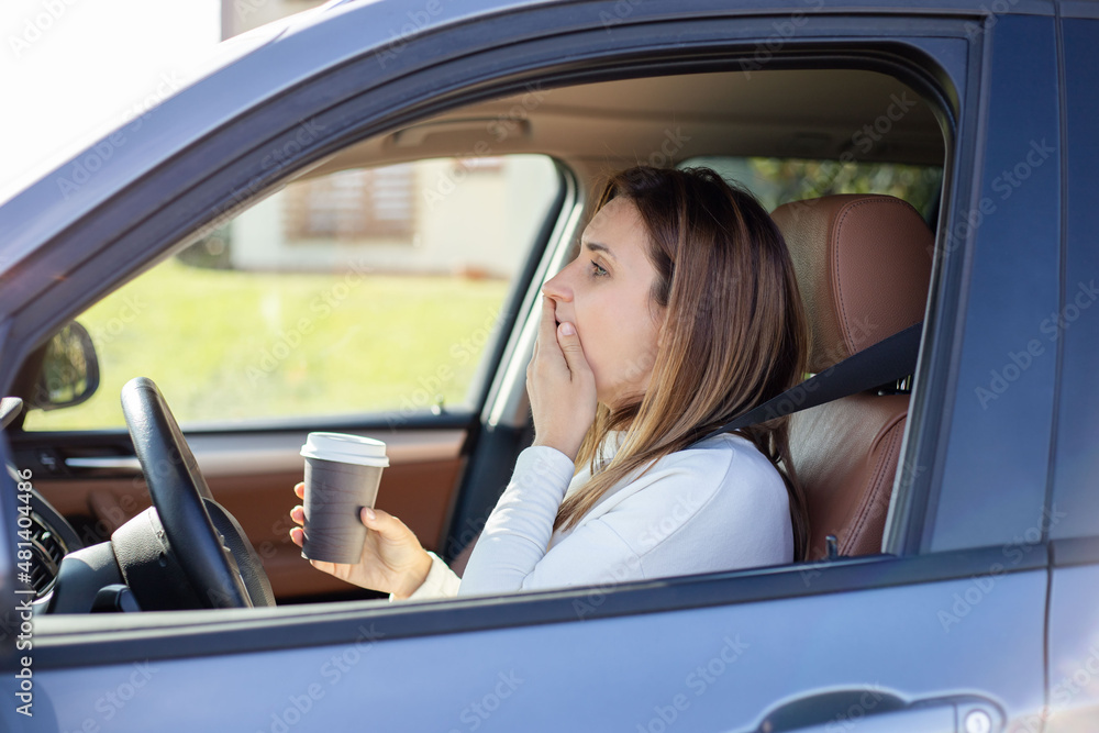 Young woman with coffee in hands  yawning in car.