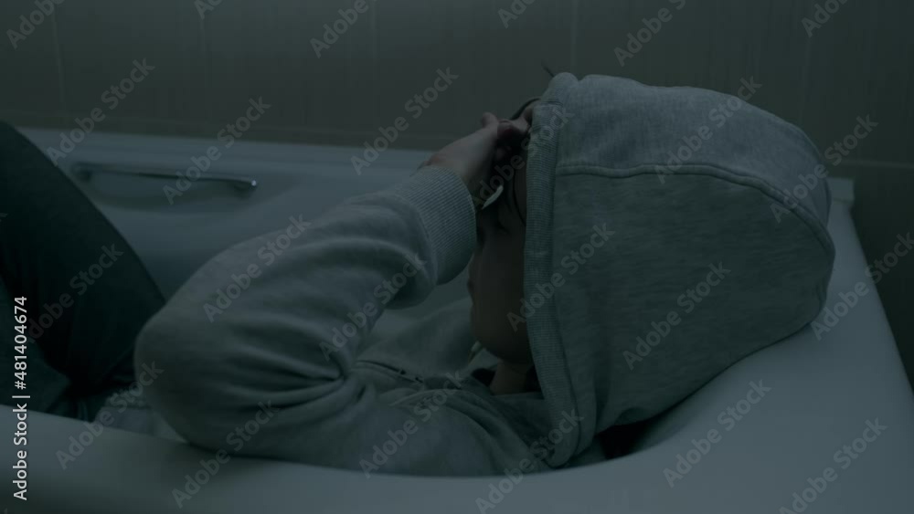 A young woman in a hood sits in a bathtub. The concept of mental and psychological health, depression. A young woman in a hood sits in a bathtub. The concept of mental and psychological health, depression.