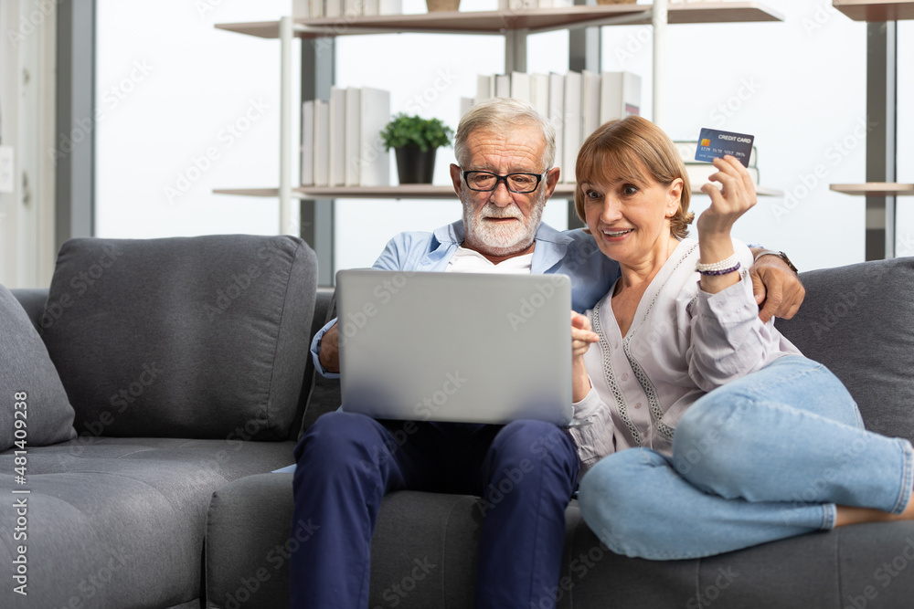 senior couple using laptop computer and credit card for shopping online on sofa