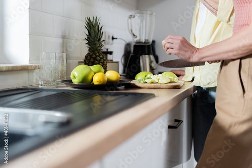 Cropped view of mature woman holding knife near fruits and husband in kitchen.