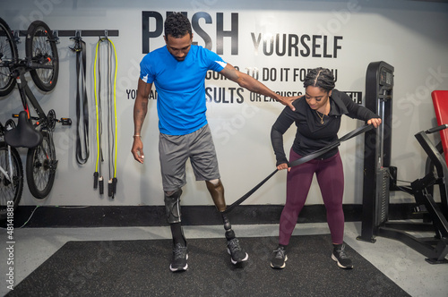 Fototapeta Naklejka Na Ścianę i Meble -  Woman assisting man with prosthetic leg exercising in gym